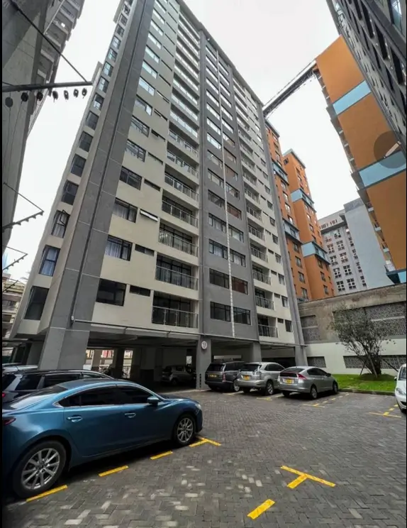 Ground-level covered parking with multiple vehicles and building facade