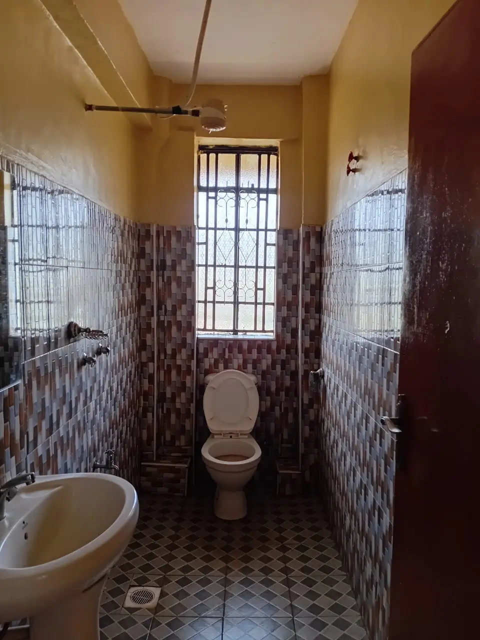 Narrow bathroom with toilet, sink, tiled walls and barred window