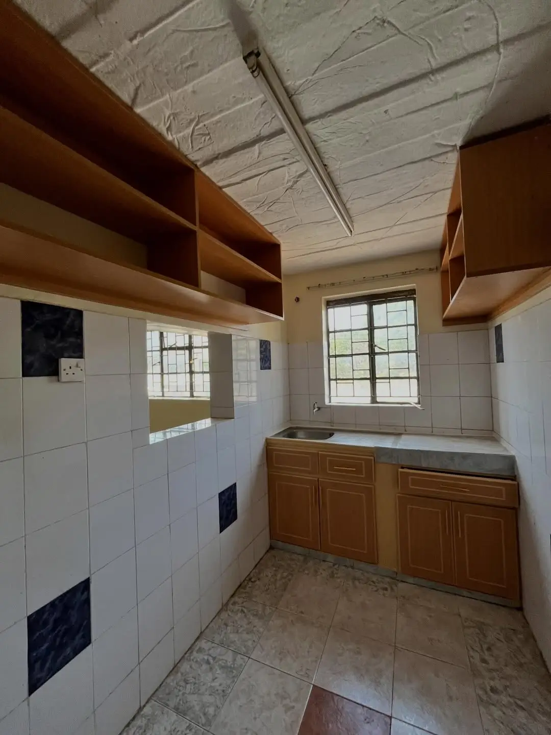 Kitchen with wooden cabinetry, white tile walls, floating shelves