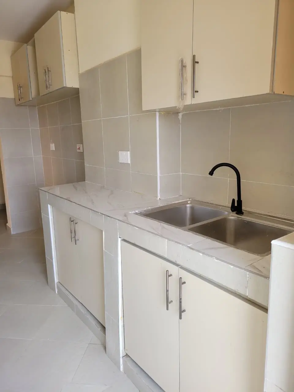 Modern kitchen with white cabinetry, dual sink, black faucet.