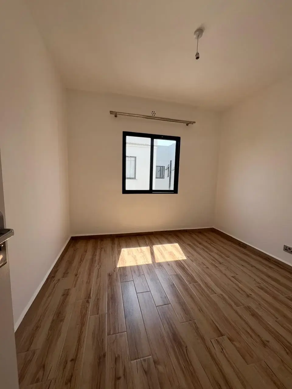 Empty bedroom with wooden flooring and window.